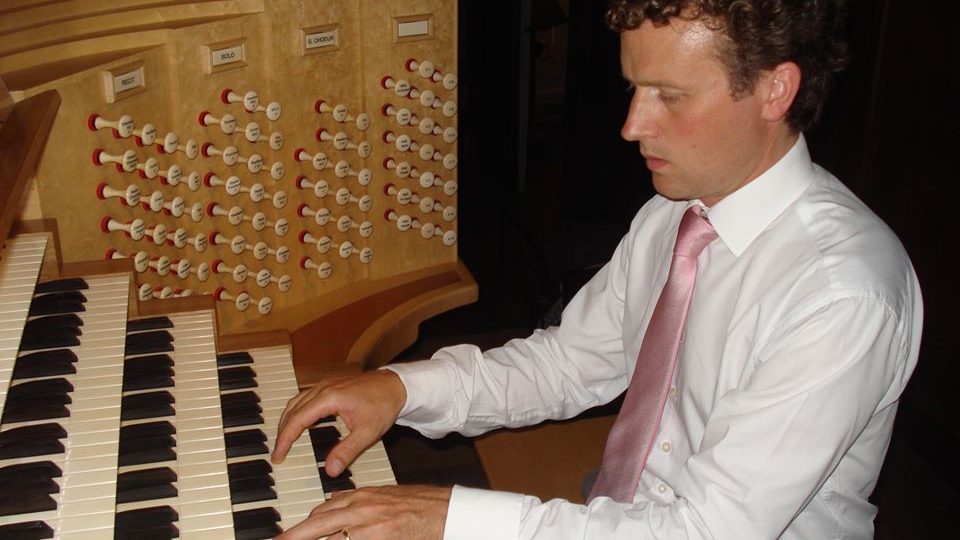 Male organist in shirt and tie, pictured in profile performing at the keyboard
